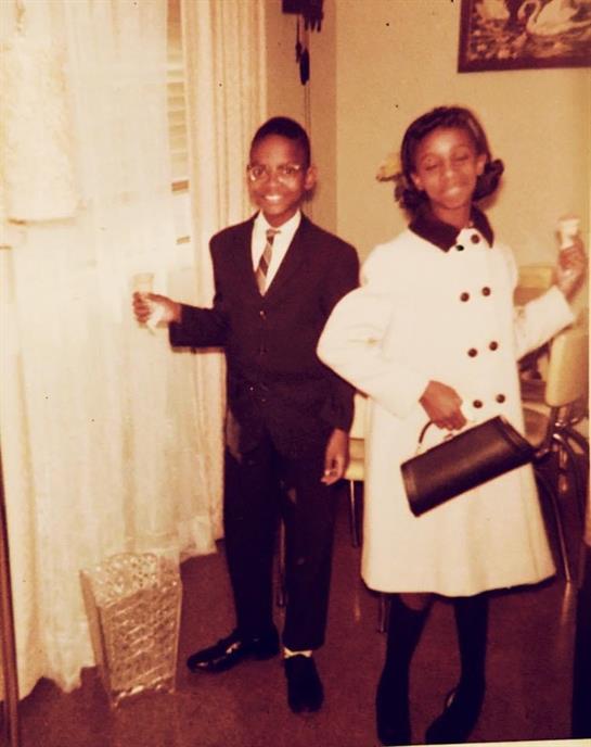 Two children stand confidently in formal clothing inside a cozy room, celebrating together.