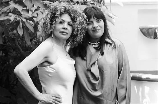 Two women stand side by side in a lush garden, exuding confidence and elegance.