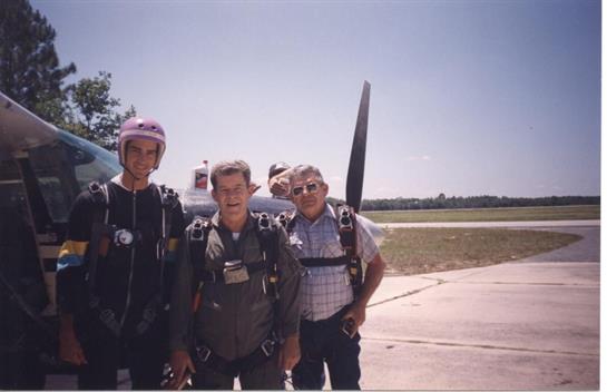 Skydivers stand together at an airfield, geared up and ready for an exciting jump on a clear day.