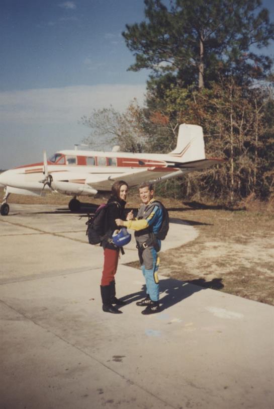 Two skydivers celebrate their landing next to a small plane on a clear day in nature.