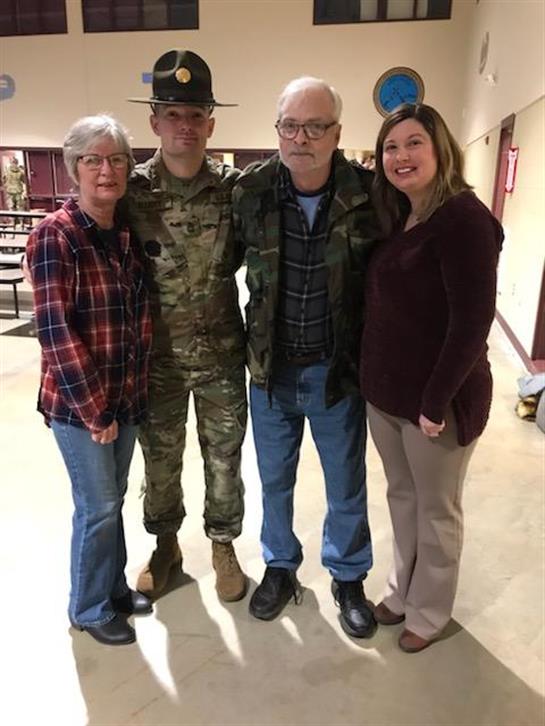 A soldier stands proudly with his family during a gathering in a community hall.