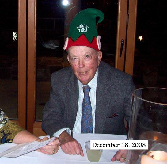 A smiling older man in a colorful hat celebrates a festive occasion with close family members.