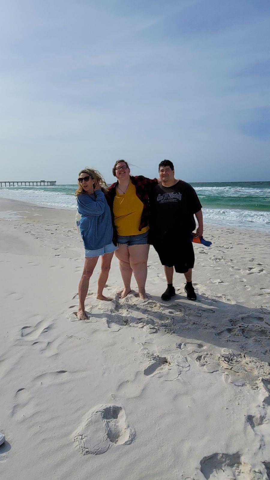 Three friends share a joyful moment on a sunny beach, embracing the waves and laughter.