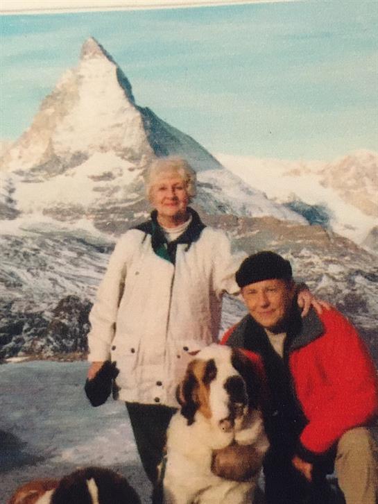 A man and woman with a dog in front of a mountain