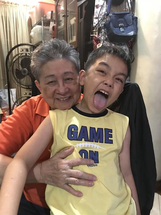 A grandmother and her grandson are having fun at home, with the boy making a playful face.
