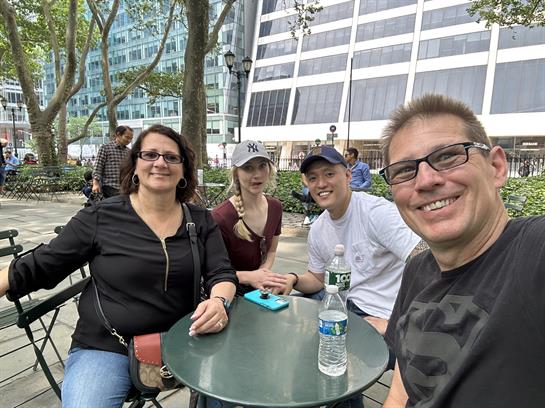 Four friends relax at a table in a bustling city park on a sunny afternoon.