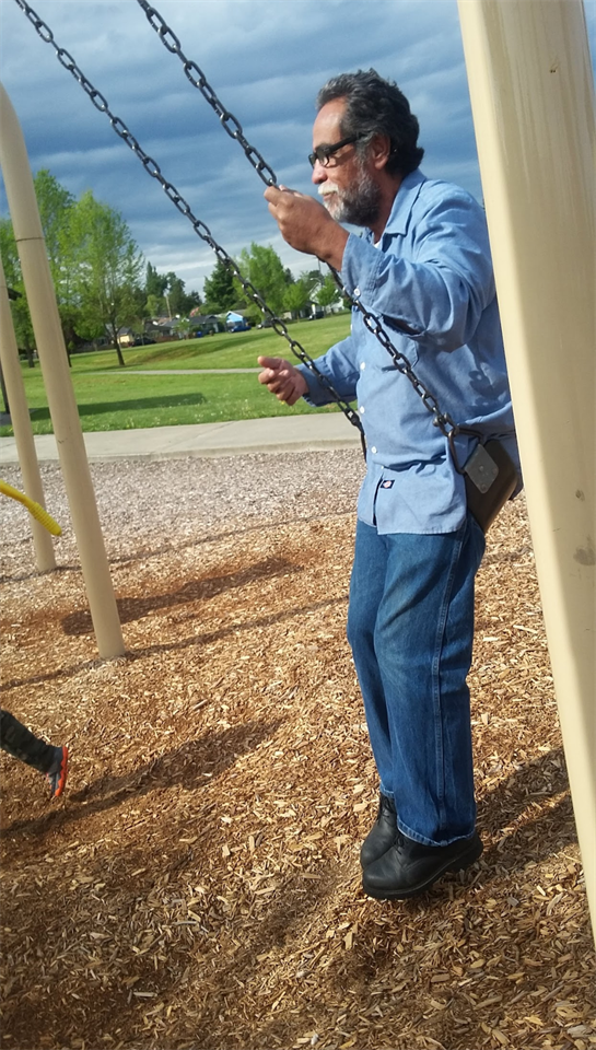 A man swings joyfully on a playground swing during a sunny afternoon in a park.