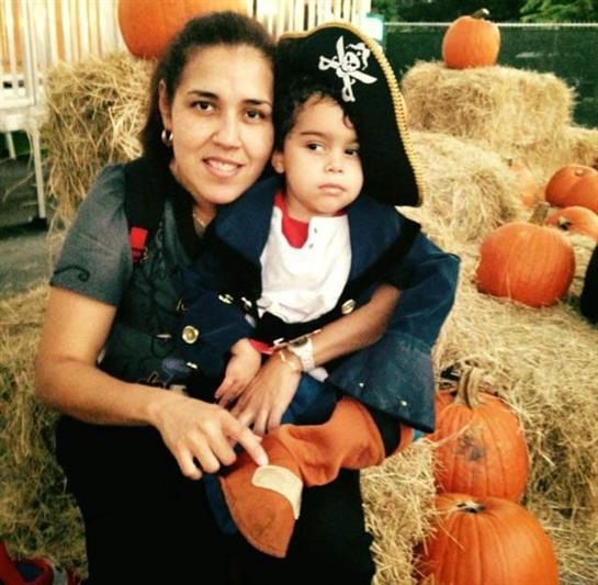 A mother holds her child wearing a pirate costume at a festive pumpkin patch.