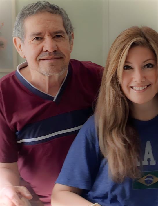 Two smiling individuals pose together in a warm, inviting space filled with natural light.
