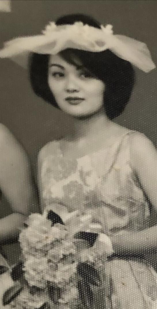 Two fashionable women wearing stylish dresses hold floral arrangements at a gathering.