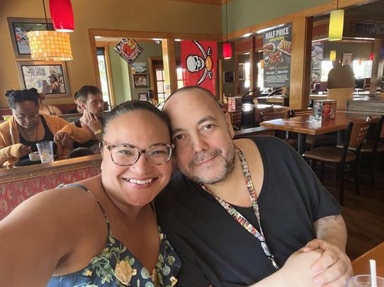 A joyful couple poses for a selfie while dining in a lively restaurant setting.