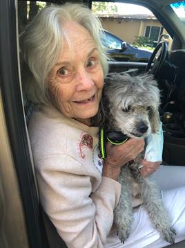 Elderly woman smiles widely while embracing her poodle in a parked car.