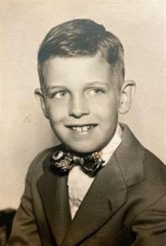 A young boy wearing a suit and bow tie smiles brightly, captured in classic vintage style.