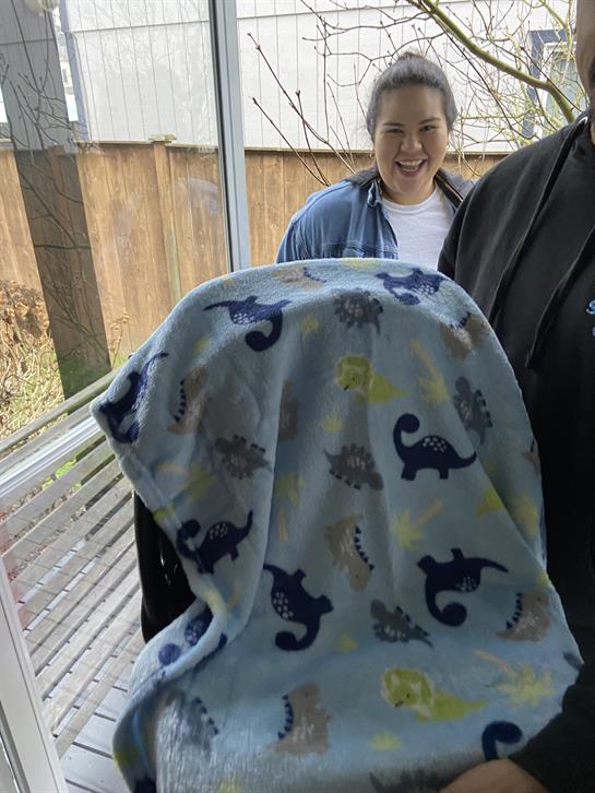 People gather indoors, sharing laughter as a child playfully snuggles in a cozy blanket.