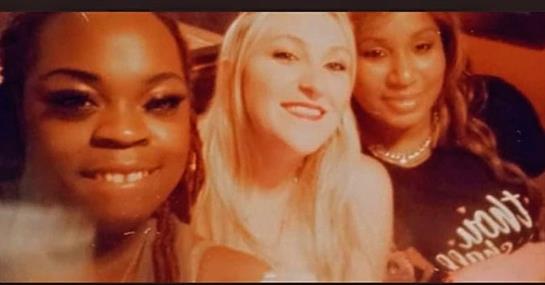 Three friends smile together, capturing a moment of joy at a lively evening event.