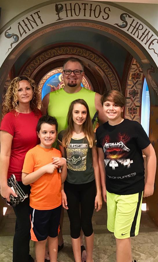 A cheerful family stands smiling indoors, surrounded by decorative elements and bright colors.
