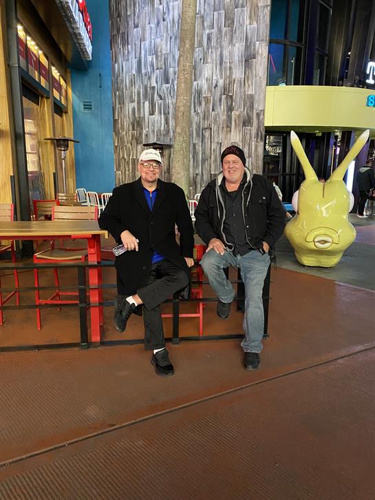 Two men sit comfortably on red benches in a vibrant indoor area, enjoying their time together.