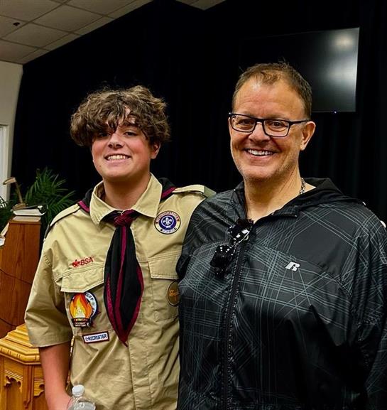 A proud young scout smiles with their supportive mentor at an achievement event.