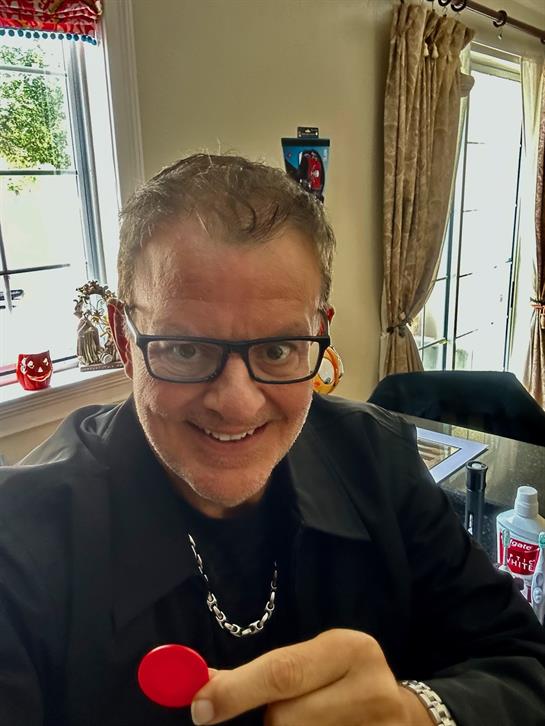 A cheerful person takes a selfie in a well-lit room with decor and natural light.