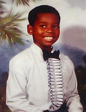A happy young boy dressed in a tuxedo stands proudly in a colorful celebration backdrop.