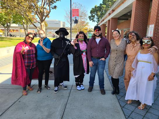 People in various costumes pose together outdoors at a festival on a bright day.