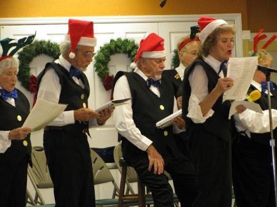A group of senior singers in holiday attire joyfully performs seasonal music at a local event.