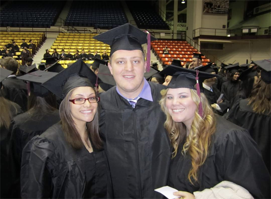 Three graduates joyfully pose in caps and gowns, celebrating their achievement indoors.