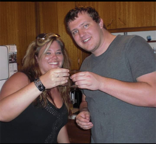 Two friends raise glasses and smile in a warm kitchen, clearly enjoying their time together.