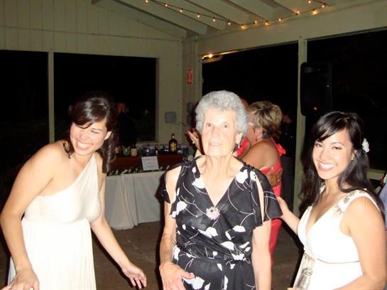 Smiling elderly woman dances with young women during a joyful celebration at a lively event.