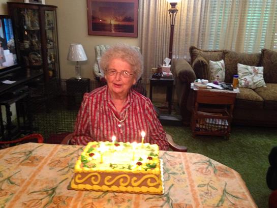 An elderly woman celebrates her birthday with a colorful cake in a cozy living room.
