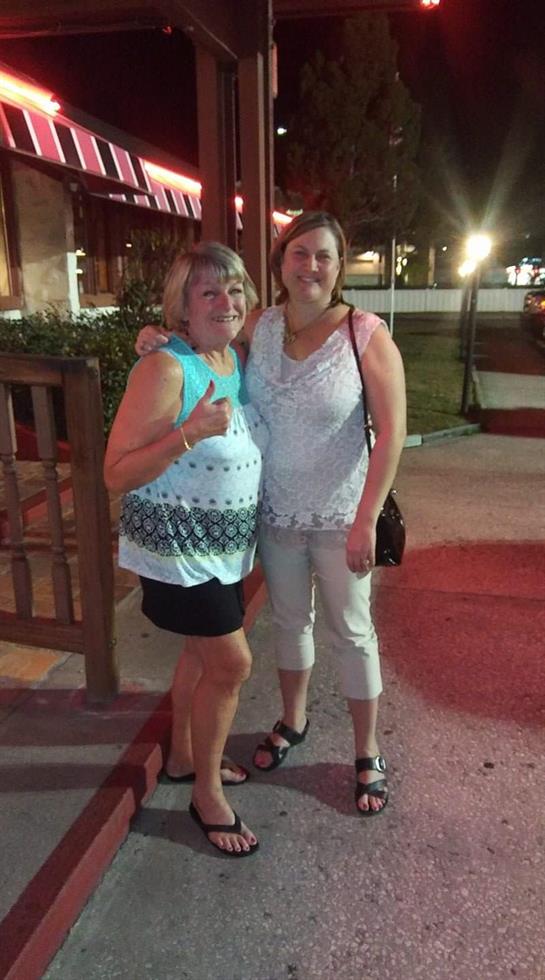 Two women pose happily outdoors in warm weather, enjoying their time together at night.