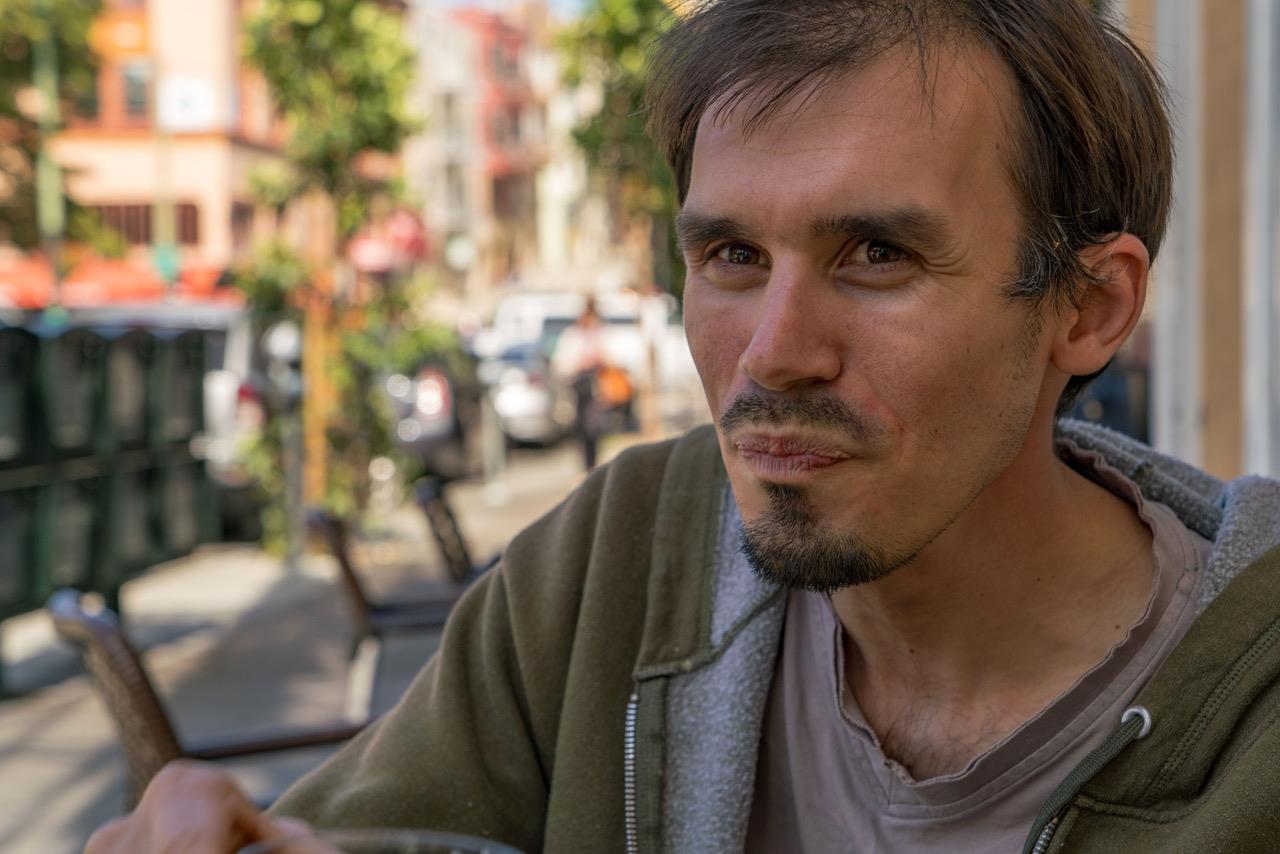 A man savors his food while seated outside at a café, surrounded by a lively cityscape.