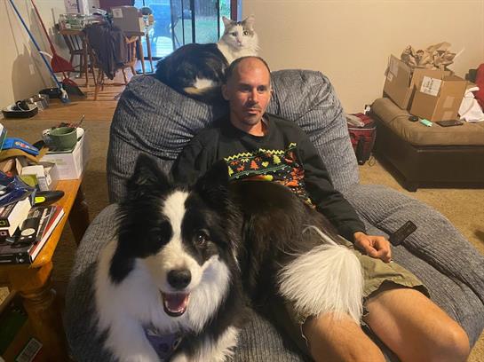 A man sits on a couch with a dog and a cat nearby, enjoying a cozy evening indoors.