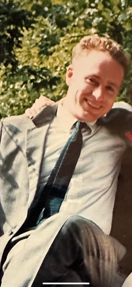 Two men in suits smile and pose together under the sunlight, enjoying their time at a gathering.