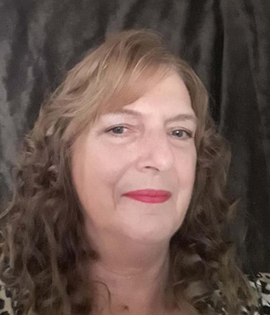 A confident middle-aged woman with curly hair smiles against a dark background.