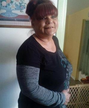 A friendly woman stands inside her home, wearing casual clothing and smiling warmly.