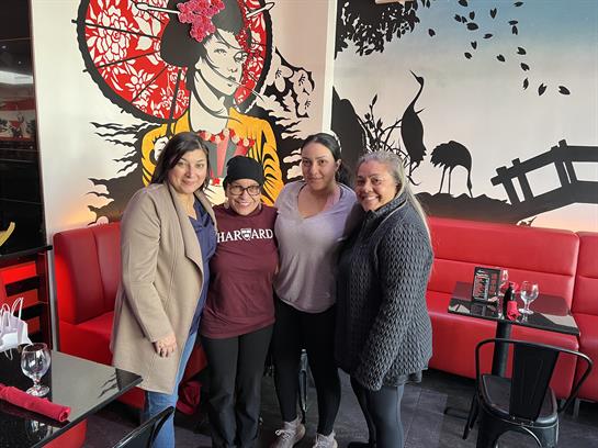 Four women stand together at a cafe featuring lively wall art, enjoying their time indoors.