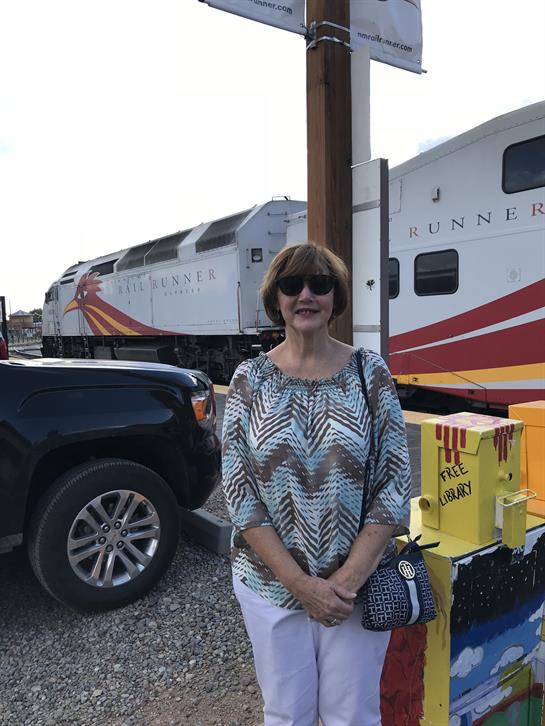 A smiling woman stands by a locomotive on a bright, cheerful day at the station.