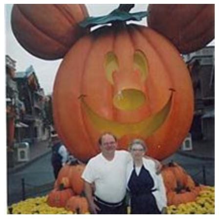 A man and woman standing in front of a large pumpkin