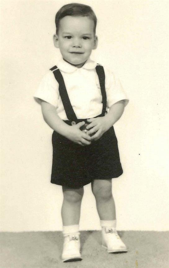 A young child stands confidently with hands on hips, smiling cheerfully.