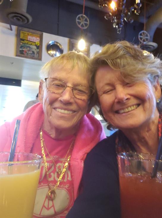 Two close friends share smiles and colorful beverages at a vibrant cafe, enjoying a joyful moment.