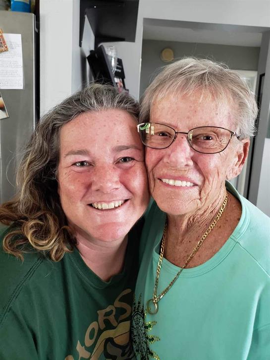 Two women share a joyful moment, embracing and smiling at each other in a cozy home setting.
