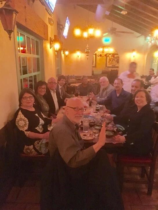 Guests are seated around a table, enjoying food and drinks in a cozy setting with warm lights.