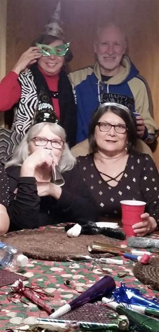 Two friends enjoy a celebratory gathering wearing party hats, surrounded by others and drinks.