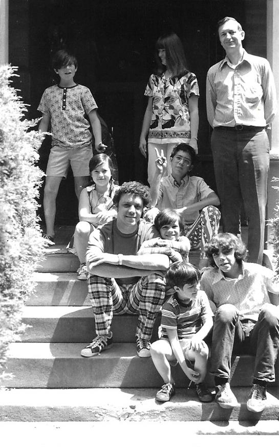 A happy group of kids and adults relaxes on house steps, enjoying each other's company.