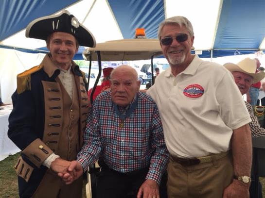 Three men smile and shake hands together at a lively historical event in a large tent.