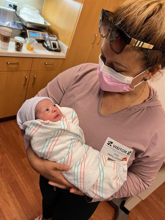 A family member holds a newborn baby wrapped in a blanket in a hospital room.