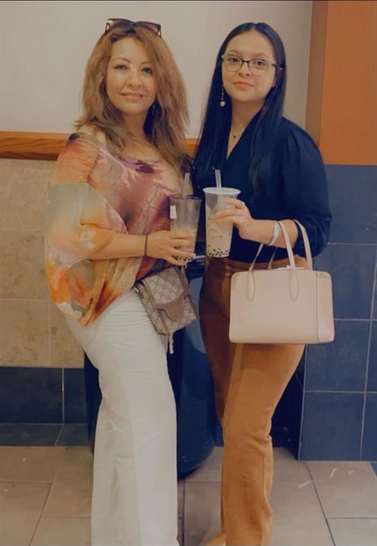 Two women stand together, sharing smiles and drinks, in a warm and lively atmosphere.