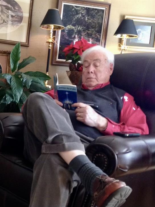 An older gentleman sits comfortably in an armchair, absorbed in a book during the holiday season.