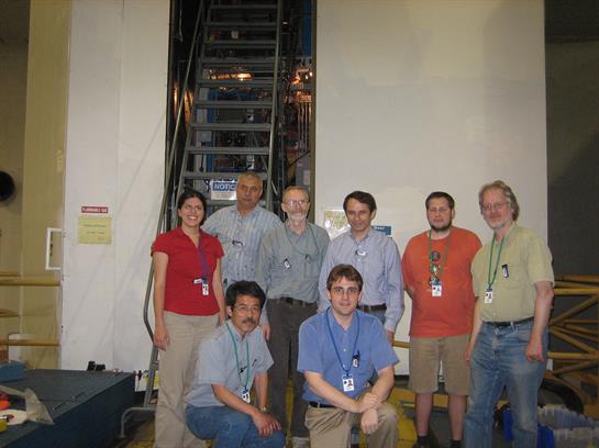 A diverse group of eight professionals poses together, smiling in a workplace setting.